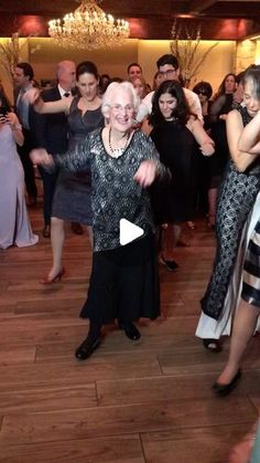 an older woman is dancing on the dance floor with other people around her and another person standing behind her