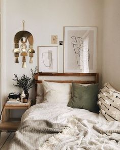 a bed with white sheets and pillows in a bedroom next to a wooden shelf filled with plants