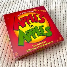 a game box sitting on top of a bed with the title apples to apples in it