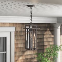 an outdoor light hanging from the ceiling in front of a house with a potted plant