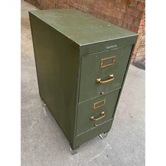 a green filing cabinet sitting on top of a sidewalk next to a brick wall and door