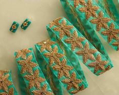 several pieces of green and gold brocaded fabric on a white surface with two pairs of earrings