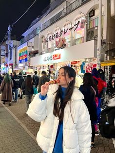 a woman is standing on the sidewalk eating something in front of a store at night