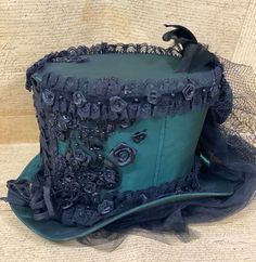 This is elegant Victorian gothic Hand made Bottle green satin Top hat with black back beautifully hand crafted feathers and bows black net bustle train.Top Hat with Black laces and 3D silk flowers and black pearls and jewels and sequences hand stitched. There is brass buckle at the side.Please refer to the photos.This is stunning Victorian Steampunk Handmade top hat made with lots of love.It is very well made, this hat is made of a Black satin type of fabric and the inside of the hat is has a Bl Fitted Fantasy Costume Hats For Themed Events, Victorian Fitted Hats For Costumes, Victorian Fitted Costume Hats, Victorian Style Fitted Costume Hats, Fitted Steampunk Top Hat For Themed Events, Steampunk Fitted Top Hat For Costume, Steampunk Fitted Top Hat For Themed Events, Fitted Gothic Costume Hats And Headpieces For Cosplay, Gothic High Crown Costume Accessories For Themed Events