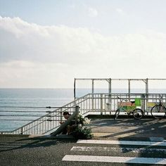 two people sitting on the edge of a pier by the ocean with bicycles parked in front of them