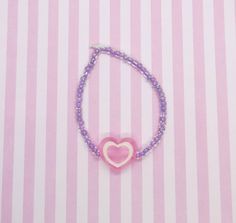 "Valentine's Day candy heart bracelet! Shiny purple beads with a big candy heart charm. Handmade by me. About 8\" in length. Strung on strong elastic cord. The cord is very sturdy but stretching it too much will eventually lead to breakage so handle with care. More pastel rainbow chokers / necklaces available in my shop! Not for babies or very young kids as the small beads are a choking hazard." Purple Heart Charm Bracelet For Valentine's Day, Valentine's Day Purple Bracelet With Heart Charm, Purple Heart Bracelet For Valentine's Day, Cute Heart Beads Charm Bracelet, Cute Heart-shaped Charm Bracelet With Heart Beads, Purple Heart Bracelets With Heart Beads, Cute Purple Heart Beads Jewelry, Purple Heart-shaped Bracelet With Heart Beads, Cute Purple Charm Bracelet For Friendship