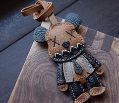 a leather keychain with a stuffed animal on it's side, sitting on top of a wooden board