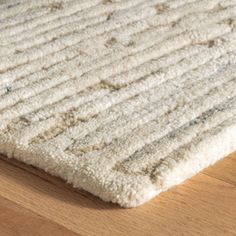 a white rug is laying on the floor with wood in the foreground and light brown hardwood floors