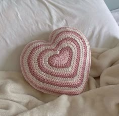 a crocheted heart shaped pillow laying on top of a white bed cover with pillows