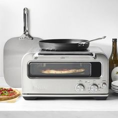 a toaster oven sitting on top of a counter next to plates and pizza cutters