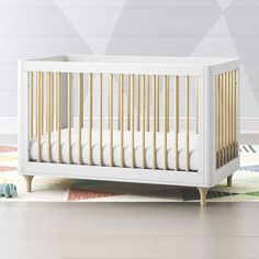 a white crib with wooden slats on the floor in front of a wall