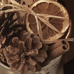 oranges, cinnamon sticks and pine cones are in a metal pail filled with dried fruit