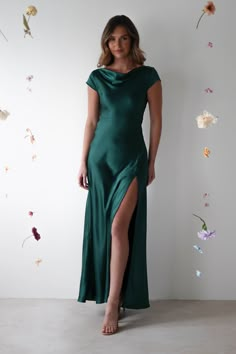 a woman in a long green dress standing against a wall with flowers on the walls