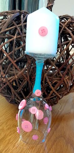 a wine glass sitting on top of a wooden table next to a vase filled with pink buttons