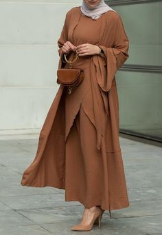 Introducing the Deluna three piece maxi lightweight abaya in rustic brown. This elegant and versatile design is perfect for any season and includes a long sleeve slip dress, apron piece, and a throw over abaya. The fabric is specially designed to resist wrinkles and the contrast brown color overlook seam at the edge of the abaya stands out.The abaya is super lightweight and flowy making it perfect for hot weather. The apron piece allows you to adjust the fit and the pattern of the abaya is not o Long Sleeve Brown Sets For Fall, Brown Long Sleeve Sets For Fall, Elegant Long Sleeve Brown Abaya, Elegant Brown Thobe For Eid, Elegant Long Thobe For Fall, Modest Solid Color Floor-length Abaya, Modest Maxi Length Abaya For Fall, Modest Floor-length Abaya, Fall Season Modest Maxi Length Abaya