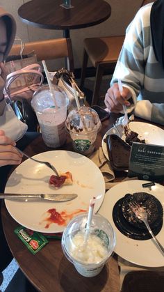 two people sitting at a table with plates and cups on it, one has food in front of the other