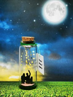 a glass jar filled with stars sitting on top of a lush green field under a full moon