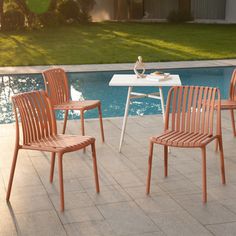 three wooden chairs sitting next to a swimming pool in front of a white table and chair