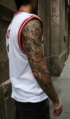 a man with a tattoo on his arm standing next to a building and looking at the street