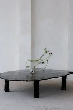 a black table with some flowers on it in front of a white wall and floor