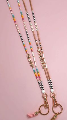 three lanyards on a pink background one has a heart charm and the other has a keychain