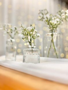 three glass vases with flowers in them sitting on a tablecloth covered table cloth