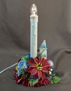 a white candle with red and green flowers on it next to a christmas ornament