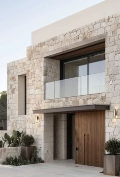 a modern house with stone walls and wooden front door, surrounded by potted plants