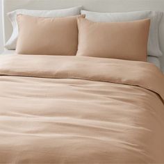 an unmade bed with beige sheets and pillows