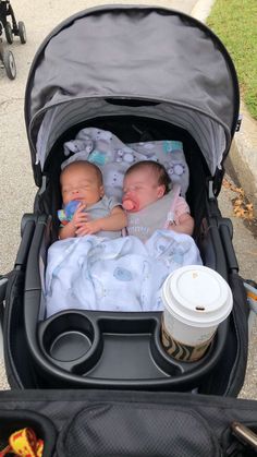 two baby babies in a stroller next to a coffee cup on the side walk