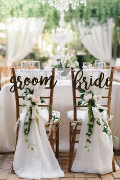 two wooden chairs with white sashes and flowers on them, sitting next to each other