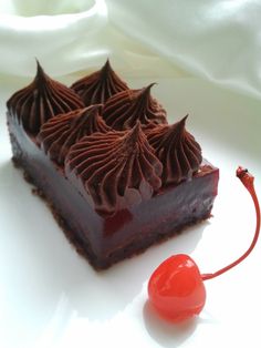 a piece of chocolate cake sitting on top of a white plate next to a cherry