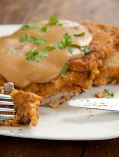 a white plate topped with meat and gravy covered in gravy next to a fork