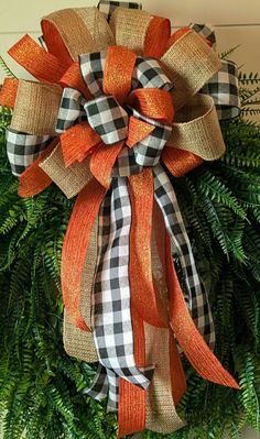 an orange and black bow hanging on the side of a door with greenery around it