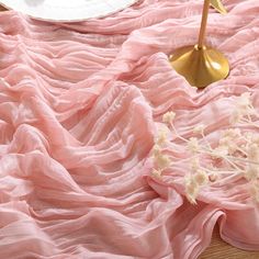 a pink blanket with white flowers on it next to a gold table lamp and plate