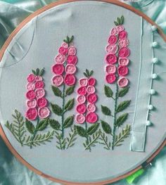 a close up of a embroidery on a piece of cloth with pink flowers and green leaves