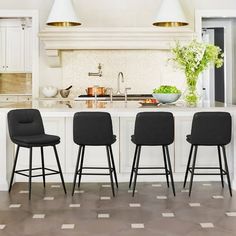 three black chairs sitting in front of a white kitchen island with marble counter tops and gold pendant lights