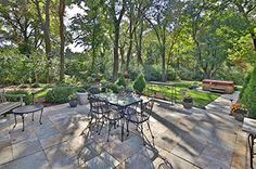 an outdoor patio with tables and chairs in the middle, surrounded by lush green trees