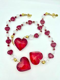 two red heart shaped necklaces on a white surface with gold accents and crystal beads