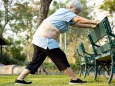 an older man pushing a green park bench in the grass with his hands on it