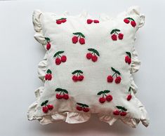 a white pillow with red cherries and green leaves on the front, sitting on a table