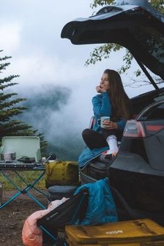 a woman sitting in the back of a car next to a camping table with food on it