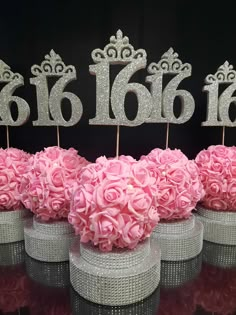 there are pink flowers in vases with silver numbers on the top and one has a tiara