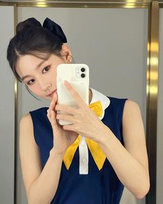 a woman taking a selfie in front of a mirror wearing a blue dress and yellow bow