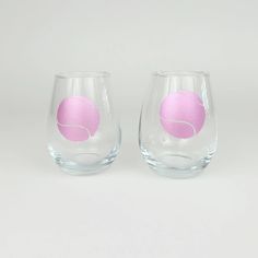 two wine glasses with pink designs on them sitting side by side in front of a white background