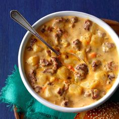 a white bowl filled with meat and cheese soup next to a baguette roll