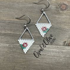 two triangle shaped earrings with white and red beads on them, hanging from silver hooks