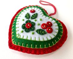 a heart shaped ornament with red buttons and green leaves