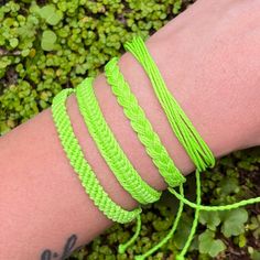 a person's arm with four different bracelets on it and green grass in the background