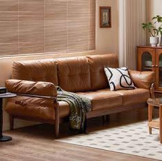 a brown leather couch sitting in a living room next to a wooden table and chair